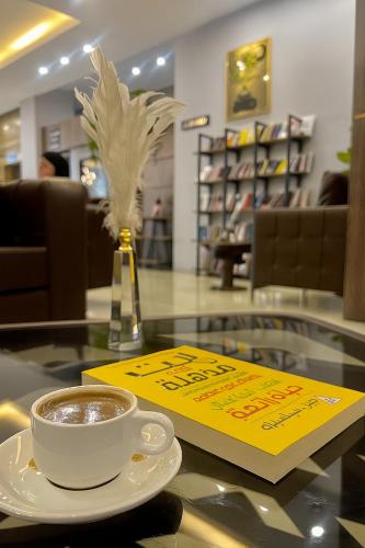 a cup of coffee on a glass table with a sign at Perlina Hotel Erbil in Erbil