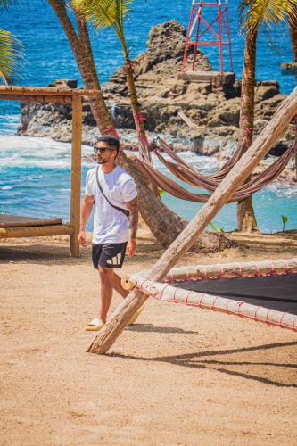 a man walking on the beach next to hammocks at El Fin del estres Sapzurro in Sapzurro