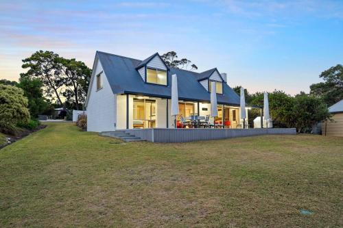 a house with a blue roof and a yard at Cliff-Top Retreat Ocean Views in Spring Beach