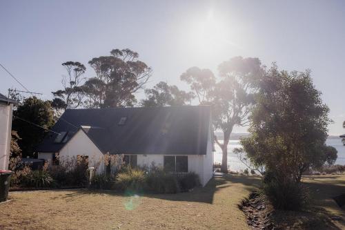 a white house with a black roof and trees at Cliff-Top Retreat Ocean Views in Spring Beach