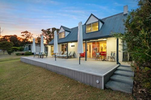 a home with a large deck with tables and chairs at Cliff-Top Retreat Ocean Views in Spring Beach