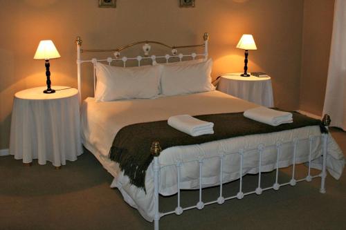 a bedroom with a large white bed with two lamps at Karoopark Guest House in Graaff-Reinet