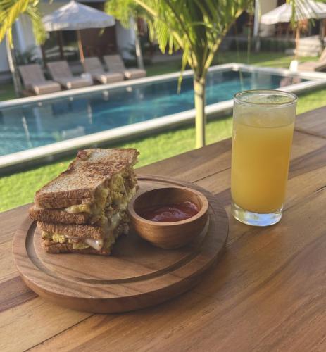 a sandwich and a glass of orange juice on a wooden table at Tropical Almond Villa in Uluwatu