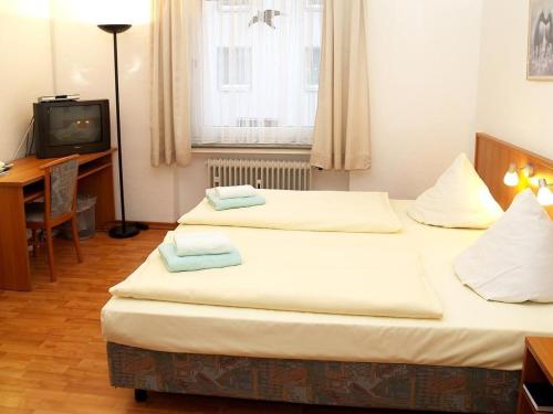 two beds in a room with a desk and a television at Altstadthotel Wienecke in Braunschweig