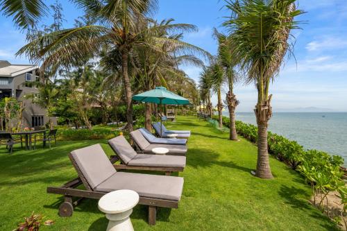 a row of chaise lounge chairs and an umbrella on the grass at Sea Lavie Boutique Resort & Spa in Hoi An