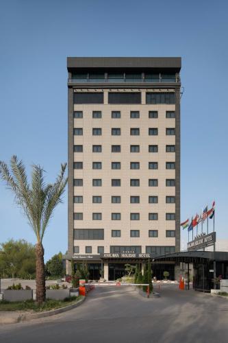 a large white building with a palm tree in front of it at Ankawa Holiday Hotel in Erbil
