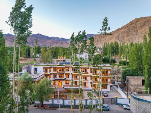 a building with trees and mountains in the background at Hotel Bayshu - The Hosteller Leh in Leh