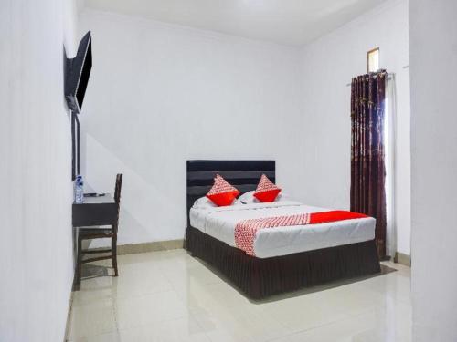 a bedroom with a bed with red pillows and a desk at Capital O 91534 Wisma Metro Permai in Makassar