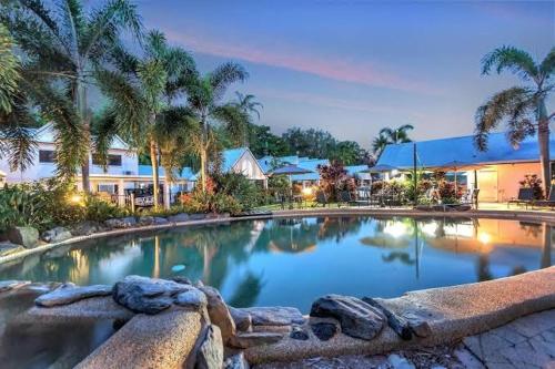 a large swimming pool with palm trees and a building at Barrier Townhouse in Port Douglas