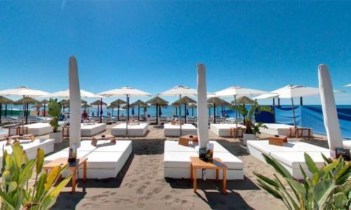 una playa con tumbonas y sombrillas blancas en SUITE PLAYA CARIHUELA Apartamentos, en Torremolinos
