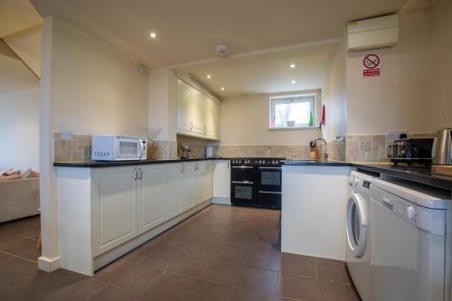 a large kitchen with white cabinets and a washer and dryer at The Barn at Brambles Farm in Bradnop