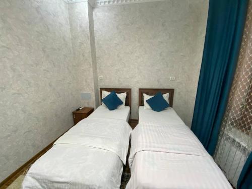 two beds in a room with blue curtains at Hotel El Emir in Samarkand