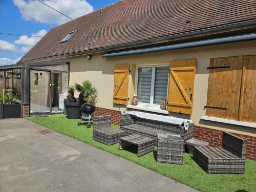 ein Haus mit einer Terrasse mit Korbmöbeln auf dem Rasen in der Unterkunft Maison dans corps de ferme Aéroport beauvais 14 minute 