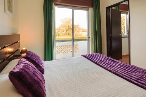sypialnia z dużym łóżkiem z fioletową pościelą i oknem w obiekcie Guest House Oliveira w mieście Boliqueime