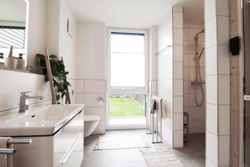 une salle de bain blanche avec un lavabo et des toilettes dans l'établissement BeltBlick 14- Küstenleuchten - Moderne Ferienwohnung direkt am Strand mit Sauna und Garten!, à Fehmarn