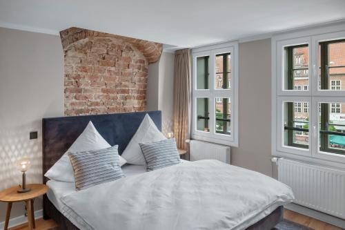a bedroom with a bed with white sheets and windows at Distillery Apartments in Lüneburg