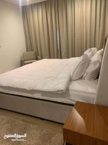 a bed with white sheets and a chair in a bedroom at شقة فندقية بمنتجع ميلينيوم in Salalah