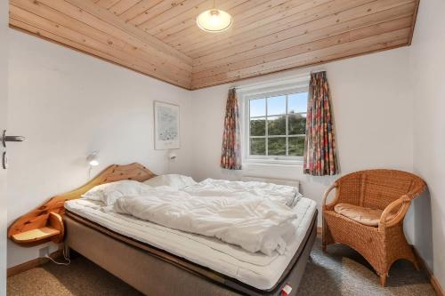 a bedroom with a bed and a chair and a window at Thatched house with pool by the sea - SJ690 in Harboør