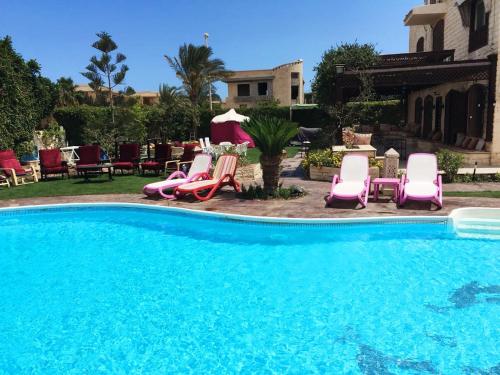 a pool with pink chairs and tables and chairs at Villa at Marassi in El Alamein