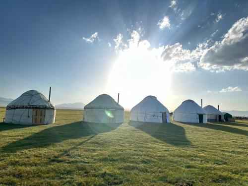 a row of tents in a field with the sun in the sky at Yurt Camp NUREL in Song-Kul