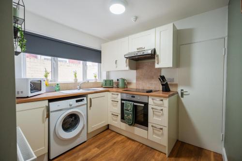 a kitchen with white cabinets and a washer and dryer at The Alfred Suite in Redcar