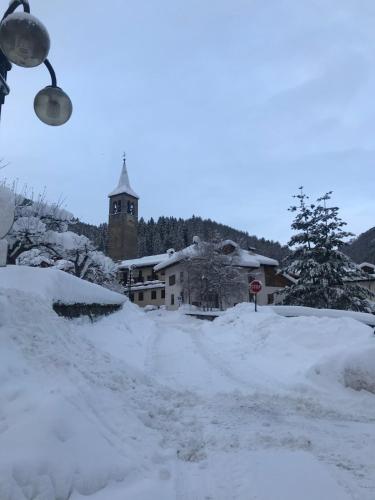 a snow covered street with a building with a clock tower at Da Nadia a Ossana casetta in Val di Sole in Ossana