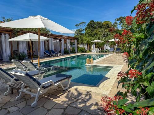 a swimming pool with chairs and an umbrella at Pousada Recanto Caxando in Trancoso