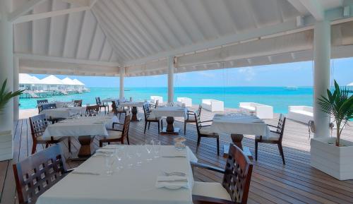 a restaurant with white tables and chairs and the ocean at Diamonds Thudufushi Maldives Resort & Spa in Thundufushi