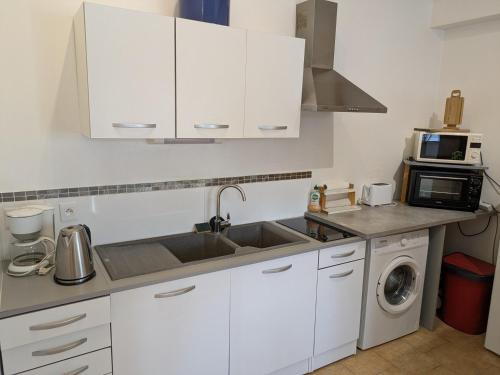 une cuisine avec des armoires blanches, un évier et un micro-ondes dans l'établissement Maison loft et jardin privatif 400m plage Royan Pontaillac, à Vaux-sur-Mer