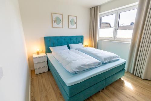 a bedroom with a bed with a blue headboard and a window at KüstenPerle - Penthousewohnung mit 2 Schlafzimmern und Sauna in Butjadingen OT Tossens