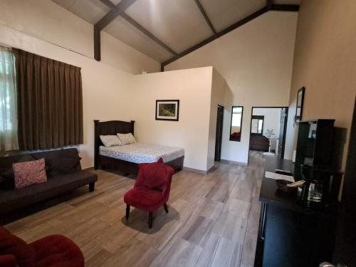 a bedroom with a bed and a couch and a red chair at La Villa Suites el Quetzal in Lanquín