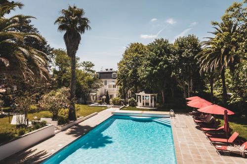 - une piscine avec des chaises et des parasols en face d'une maison dans l'établissement Parc Victoria Hôtel, à Saint-Jean-de-Luz