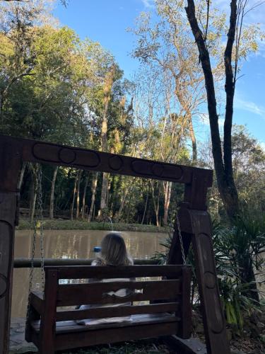 a person sitting on a bench in front of a pond at Cabanas dos Plátanos in Gramado