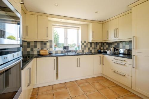 a kitchen with white cabinets and a window at 2 Hazelwood - 2 bedroom house near Aldeburgh & Snape Maltings - Aldeburgh Coastal Cottages in Aldringham