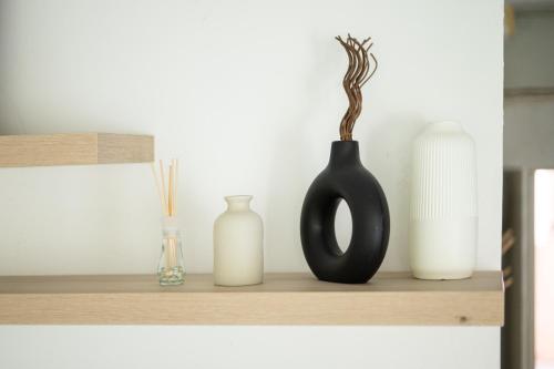 a shelf with a black vase and three white vases at Studio 91 By IsrApart in Ramat Gan