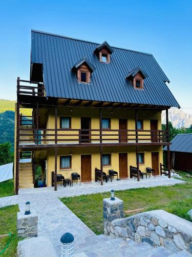 a large house with a metal roof with tables and chairs at Guesthouse Gjoni Theth in Theth