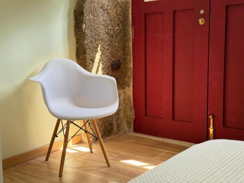 a white chair sitting in front of a red door at Refúgio Rural - Gerês in Terras de Bouro