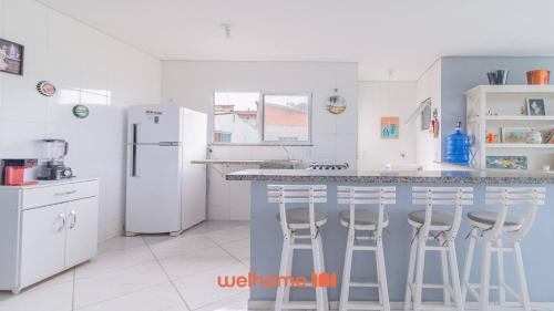 a kitchen with white appliances and a counter with stools at Apartamento em Bertioga com vista para o mar in Bertioga