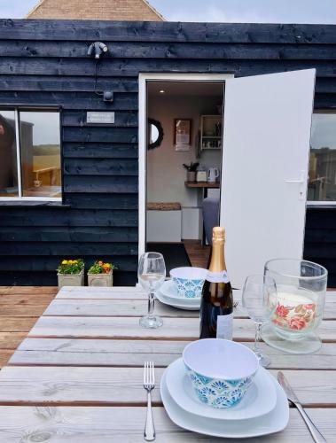 a table with plates and glasses and a bottle of wine at Unique Suffolk Cabin with Countryside Views in Burgh