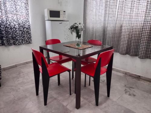 a dining room table with red chairs and a vase with flowers at Depa 11, Torre Belén, Mazatlán in Mazatlán