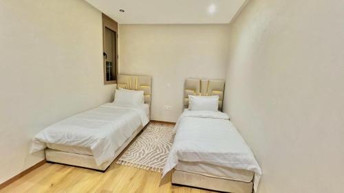 two beds in a room with white walls and wooden floors at T1 Charmant & Cosy à 10 min de Hay Riad, Accès Facile in Temara