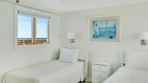 two beds in a white room with two windows at Windward Shores in Amagansett