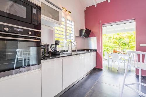 una cocina con armarios blancos y una pared rosa en Villa Alamanda à 1400 m de la mer - Jacuzzi privé, en Sainte-Anne