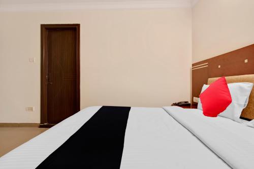 a bedroom with a large bed with a red pillow at Capital O Elegant Amethyst Business Hotel Near Ragigudda Sri Prasanna Anjaneyaswamy Temple in Bengaluru