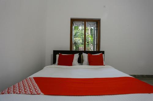 a bed with red and white pillows and a window at Hotel O Al Ameen Residency in Kannur