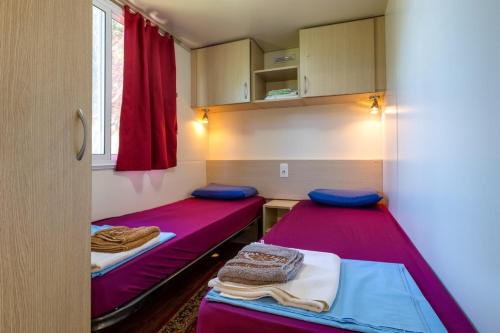 two beds in a small room with red curtains at Apartments by the sea Cove Kurila, Losinj - 24571 in Mali Lošinj