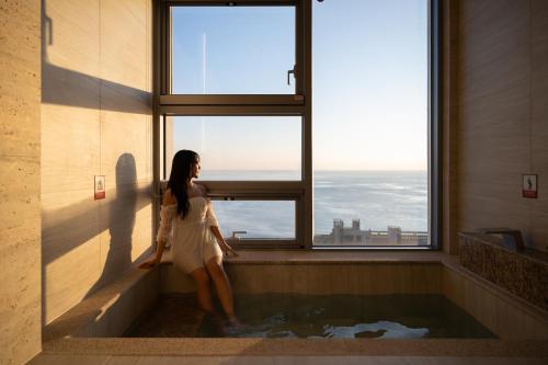 a woman sitting in a bath tub looking out a window at Mer de laube Hotel in Busan