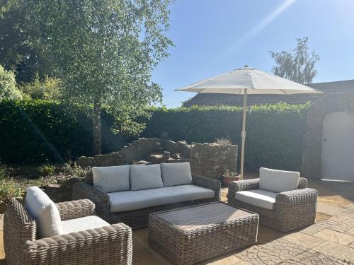 a patio with wicker chairs and an umbrella at The Old Vicarage in Hinton Saint George