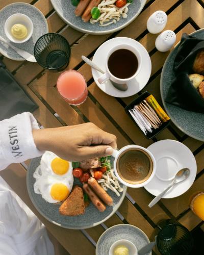 a table with plates of food and a person holding a cup of coffee at The Westin Nirup Island Resort & Spa in Belakangpandang