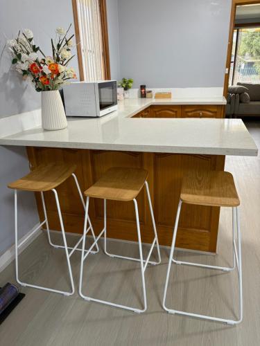 a kitchen island with two stools and a white counter top at Helen's Cosy House In Miller in Mount Pritchard